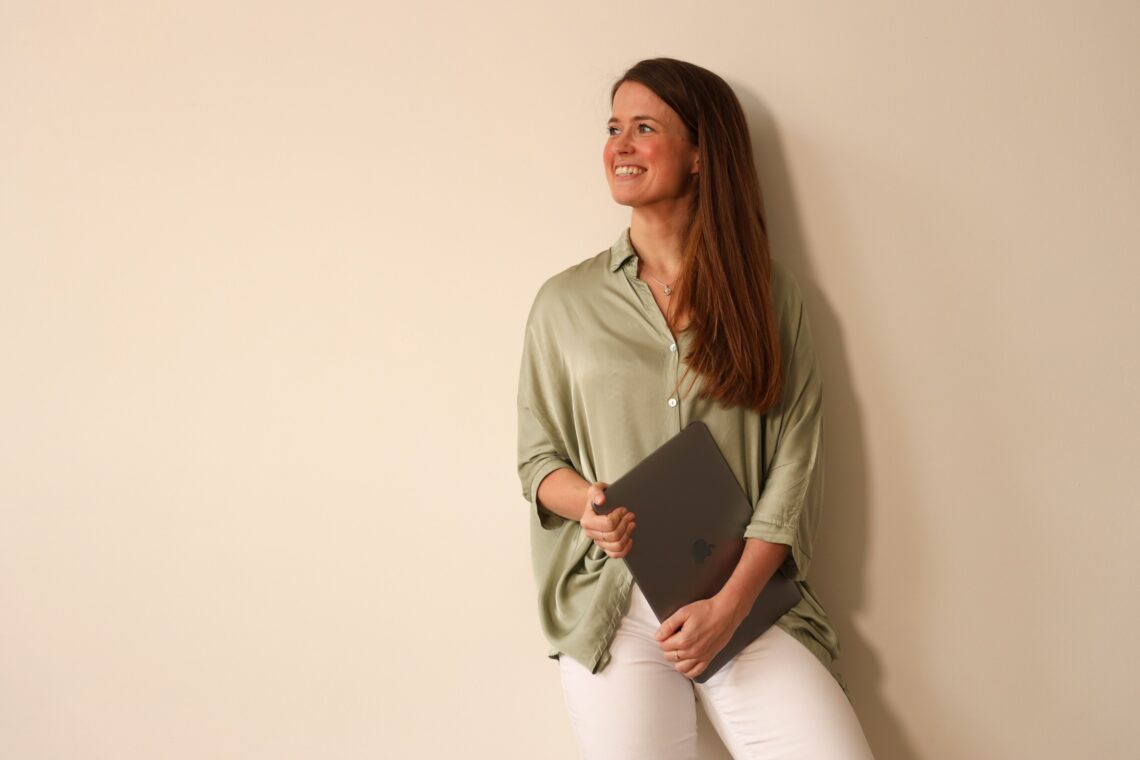 merit koutstaal met witte broek en groene blouse met laptop in hand